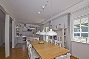 A modern kitchen with white cabinets, a wooden dining table, and pendant lights. - Vacation home Frigga - comfortable Swedish house close to the beach with sea view - (Wiek)