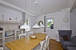 Un salon moderne avec une table à manger en bois, des chaises blanches, un canapé gris et des luminaires suspendus.