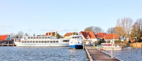 A riverfront with a dock, a large boat, and buildings with red roofs.