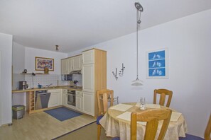 A compact kitchen with white cabinets, a dining table with chairs, and a blue rug. - Apartment near the harbor with a balcony and ocean view - Hafenhäuser Breege FeWo 14 - (Breege)