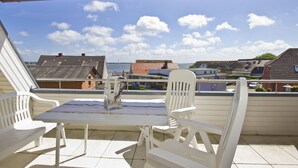 A terrace with a table and chairs, overlooking a residential area with houses and a body of water.
