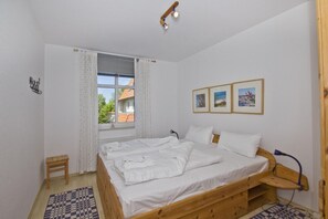 A bedroom with a wooden bed, a small bedside table, a window with curtains, and three framed pictures on the wall. - Apartment near the harbor with balcony and sea view - Hafenhäuser Breege FeWo 14 - (Breege)
