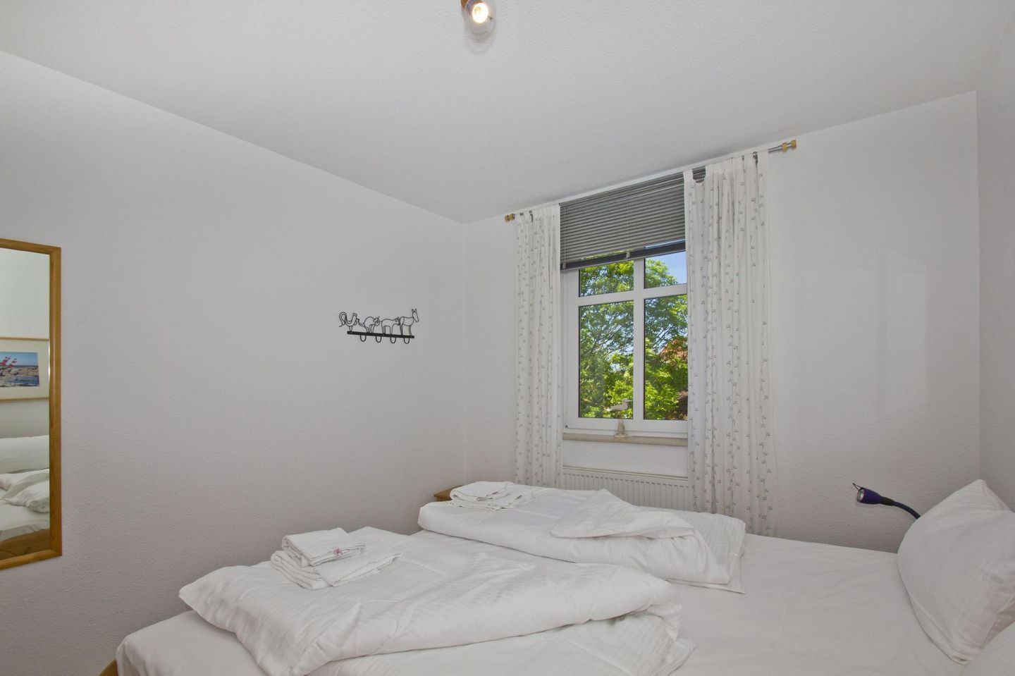 Une chambre avec deux lits, une fenêtre avec des rideaux, un luminaire fixé au mur et un petit miroir.