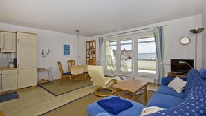A compact living space with a dining area, a sofa, a TV, and a view of the sea through large windows.