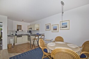 A compact kitchen with white cabinets, a dining area with wicker chairs and a table, and a ceiling fan. - Vacation apartment near the harbor with terrace and sea view - Hafenhäuser Breege FeWo 13 (Breege)