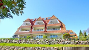 A multi-story hotel with a red-tiled roof, balconies, and a stone retaining wall in front.