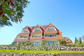 A multi-story hotel with a red-tiled roof, balconies, and a stone retaining wall in front.