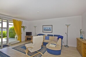 Ein Wohnzimmer mit einer Couch, einem Sessel, einem Fernseher und einer Stehlampe.