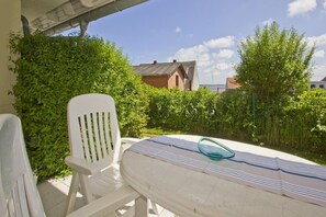 A patio with a white table and chairs, surrounded by lush greenery and a clear sky. - Vacation apartment near the harbor with terrace and sea view - Hafenhäuser Breege FeWo 13 (Breege)