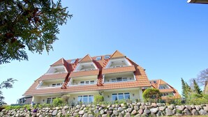A multi-story building with a red-tiled roof, balconies, and a stone wall in front. - Maisonette apartment near the harbor with sea view, balcony - Hafenhäuser Breege FeWo 06 (Breege)