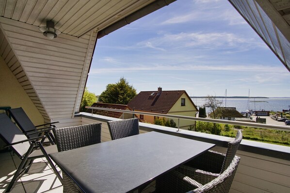 Un balcon avec une table et des chaises, donnant sur une étendue d’eau et des bâtiments.