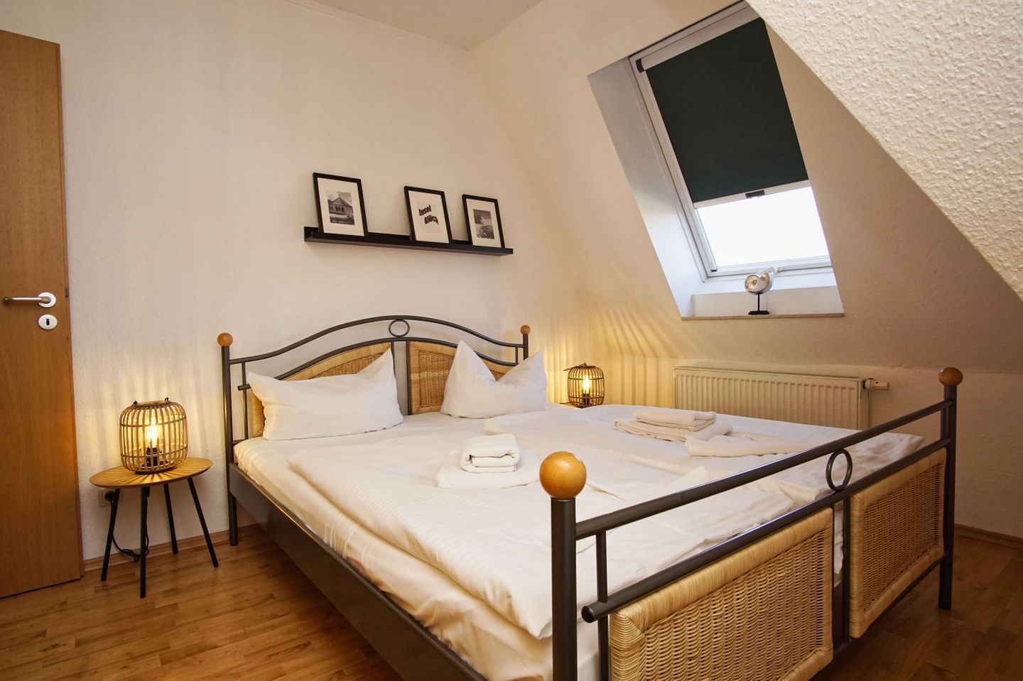 Un dormitorio con una cama, dos mesitas de noche, una ventana y una estantería en la pared con fotografías.