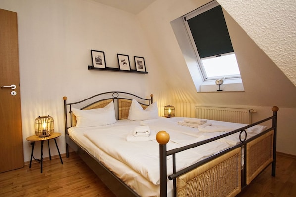 A bedroom with a bed, two bedside tables, a window, and a wall-mounted shelf with pictures.