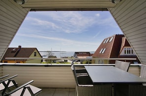 A balcony with a table and chairs, overlooking a residential area with houses and a body of water. - Duplex apartment near the harbor with a view of the sea, balcony - Hafenhäuser Breege FeWo 06 (Breege)