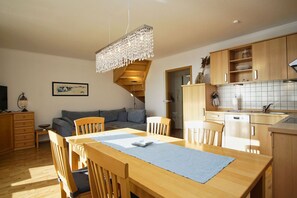 Une cuisine moderne avec des meubles en bois, un coin repas comprenant une table et des chaises, et un escalier menant à l’étage supérieur.