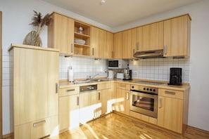 A modern kitchen with wooden cabinets, a stainless steel sink, a microwave, a coffee maker, and an oven.
