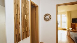 A room with a wooden slat partition, a door, a wall-mounted wreath, and a glimpse of a living area with a sofa and a television. - Maisonette apartment near the harbor with sea view, balcony - Hafenhäuser Breege FeWo 06 (Breege)