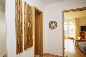 A room with a wooden slat partition, a door, a wall-mounted wreath, and a glimpse of a living area with a sofa and a television. - Maisonette apartment near the harbor with sea view, balcony - Hafenhäuser Breege FeWo 06 (Breege)