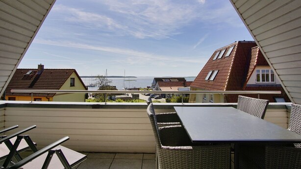A balcony with a table and chairs, overlooking a residential area with houses and a body of water. - Maisonette apartment near the harbor with sea view, balcony - Hafenhäuser Breege FeWo 06 (Breege)