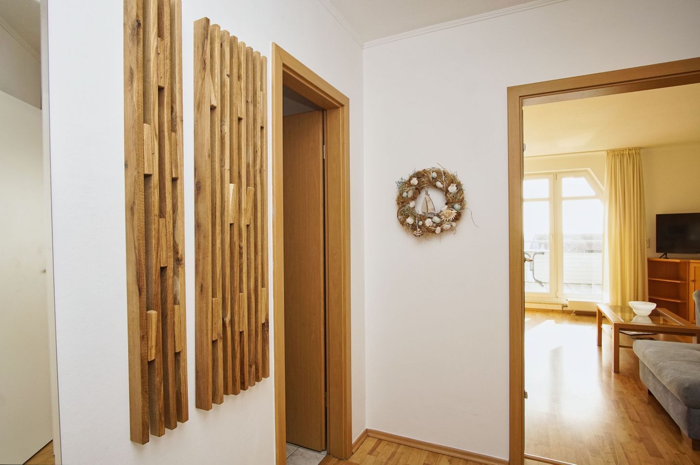 Ein Zimmer mit einer Holzhakenteilung, einer Tür, einem an der Wand befestigten Kranz und einem Blick auf eine Wohnbereich mit Sofa und Fernseher.