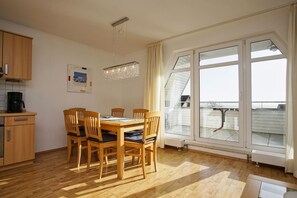 A dining area with a wooden table and chairs, a chandelier, and a large window with a view of a building.