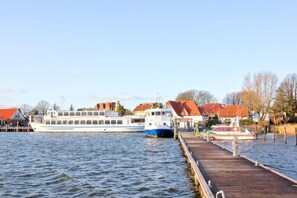 Un río con muelle, un barco grande y edificios con techos rojos.