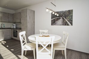 Una cocina moderna con armarios grises, una mesa de comedor blanca con cuatro sillas y una lámpara colgante.