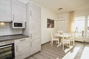 Una cocina moderna con armarios blancos, microondas integrado y un comedor con una mesa redonda y sillas blancas.