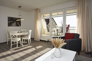 A modern living room with a dining area, large windows, and a view of a staircase. - 2-room vacation apartment near the harbor with balcony - Hafenhäuser Breege FeWo 05 - (Breege)