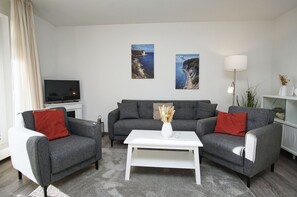 En moderne stue med en grå sofa, et hvidt sofabord og to billeder af kystlandskaber.