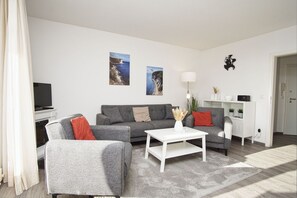 Una sala de estar moderna con un sofá gris, una mesa de centro blanca y un televisor sobre un mueble.