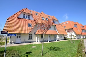 Eine Reihung von Häusern mit orangefarbenen Ziegeldächern und weißen Wänden, ein klarer blauer Himmel und ein Schild mit der Aufschrift 'Mittelstraße Am Hafen'.