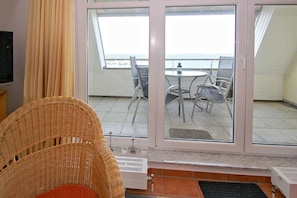 A room with a wicker chair, a television, and a view of a balcony with chairs and a table.