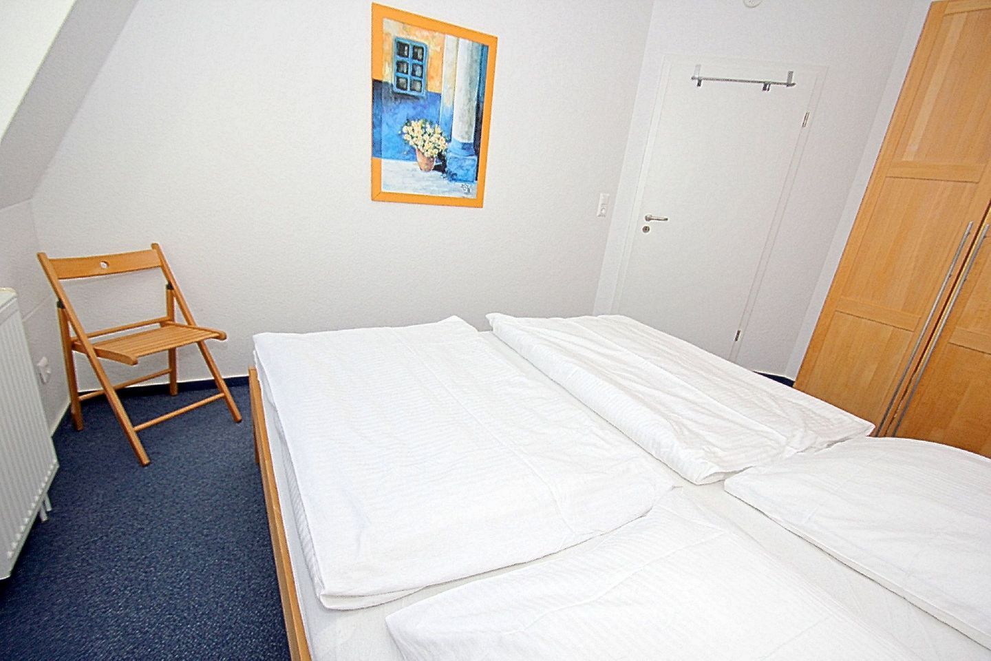 A bedroom with a bed, a wooden chair, a radiator, and a door.