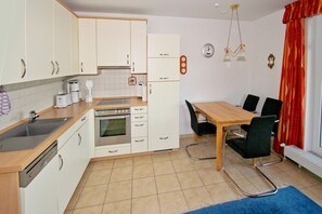 Eine kompakte Küche mit weißen Schränken, einem Einbauofen, einem Spülbecken und einem Essbereich mit Tisch und Stühlen.