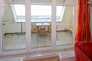 Ein Zimmer mit großem Fenster mit Blick auf ein Gewässer, einem Esstisch mit Stühlen und einem roten Sessel im Vordergrund.