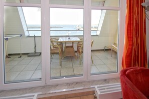Ein Zimmer mit großem Fenster mit Blick auf ein Gewässer, einem Esstisch mit Stühlen und einem roten Sessel im Vordergrund.