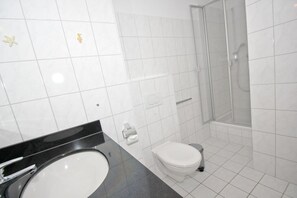A bathroom with a white toilet, a sink with a black countertop, and a glass-enclosed shower. - Apartment near the harbor with balcony and sea view - Hafenhäuser Wiek 15 - (Wiek)