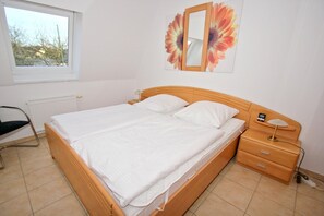 Un dormitorio con una cama individual, una mesita de noche con lámpara, una silla y una ventana.