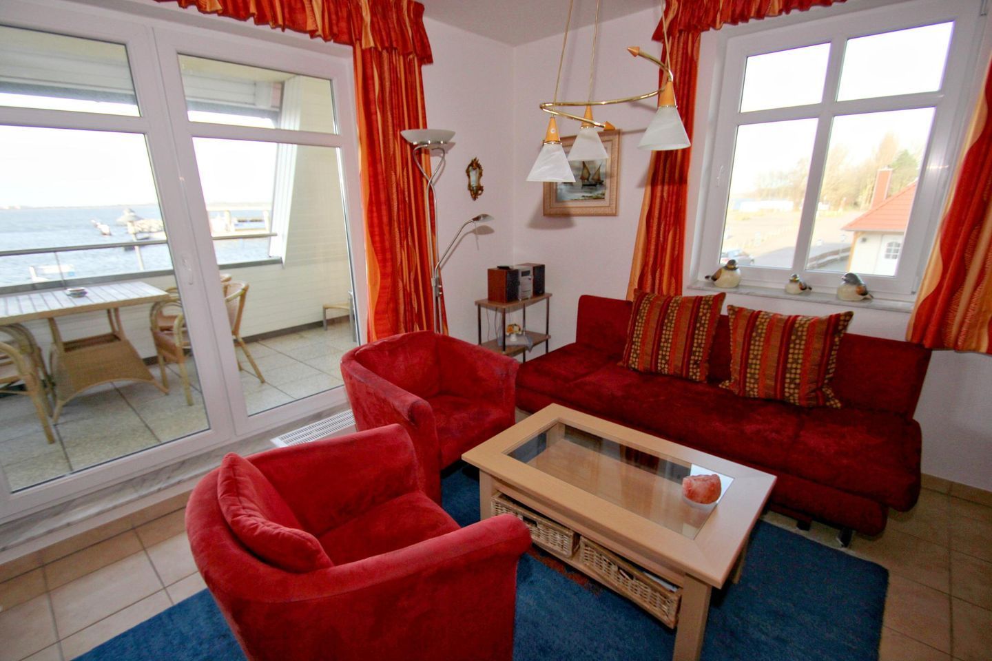 A living room with a red sofa, two red armchairs, a glass coffee table, and a view of the sea through large windows.
