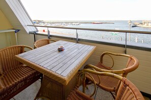 A balcony with wicker furniture, a wooden table, and a view of the water and boats. - Apartment near the harbor with balcony and sea view - Hafenhäuser Wiek 15 - (Wiek)