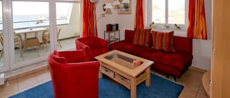 Ein Wohnzimmer mit einem roten Sofa, zwei roten Sesseln, einem Holztisch und einem großen Fenster mit Vorhängen.