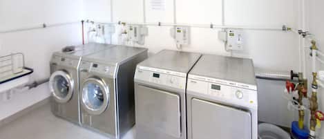 A laundry room with two front-loading washing machines and a dryer, equipped with various control panels and hoses.