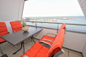 A balcony with a table and orange chairs, overlooking a marina with boats and a pier. - Apartment near the harbor with balcony and sea view - Hafenhäuser Wiek 11 - (Wiek)