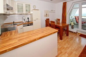 Ett kompakt kök med vita skåp, en bänkskiva i trä och en matplats med trästolar och ett bord.