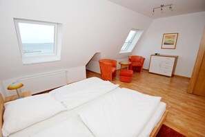 Une chambre à coucher comprenant un lit, deux chaises, une petite table, une armoire et une fenêtre donnant sur la mer.