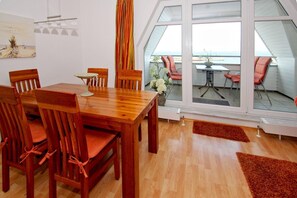 A dining area with a wooden table and chairs, large windows with a view of the sea, and a painting on the wall. - Apartment near the harbor with balcony and sea view - Hafenhäuser Wiek 11 - (Wiek)