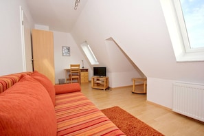 A cozy loft bedroom with a sloped ceiling, a large window, a sofa, a desk, and a TV. - Apartment near the harbor with a balcony and a view of the sea - Hafenhäuser Wiek 11 - (Wiek)