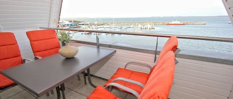 A balcony with a table and orange chairs, overlooking a marina with boats and a pier.