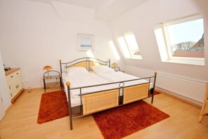 A bedroom with a metal bed frame, two bedside lamps, a white bedside table, a red rug, and a window with a view of a building. - Apartment near the harbor with balcony and sea view - Hafenhäuser Wiek 11 - (Wiek)